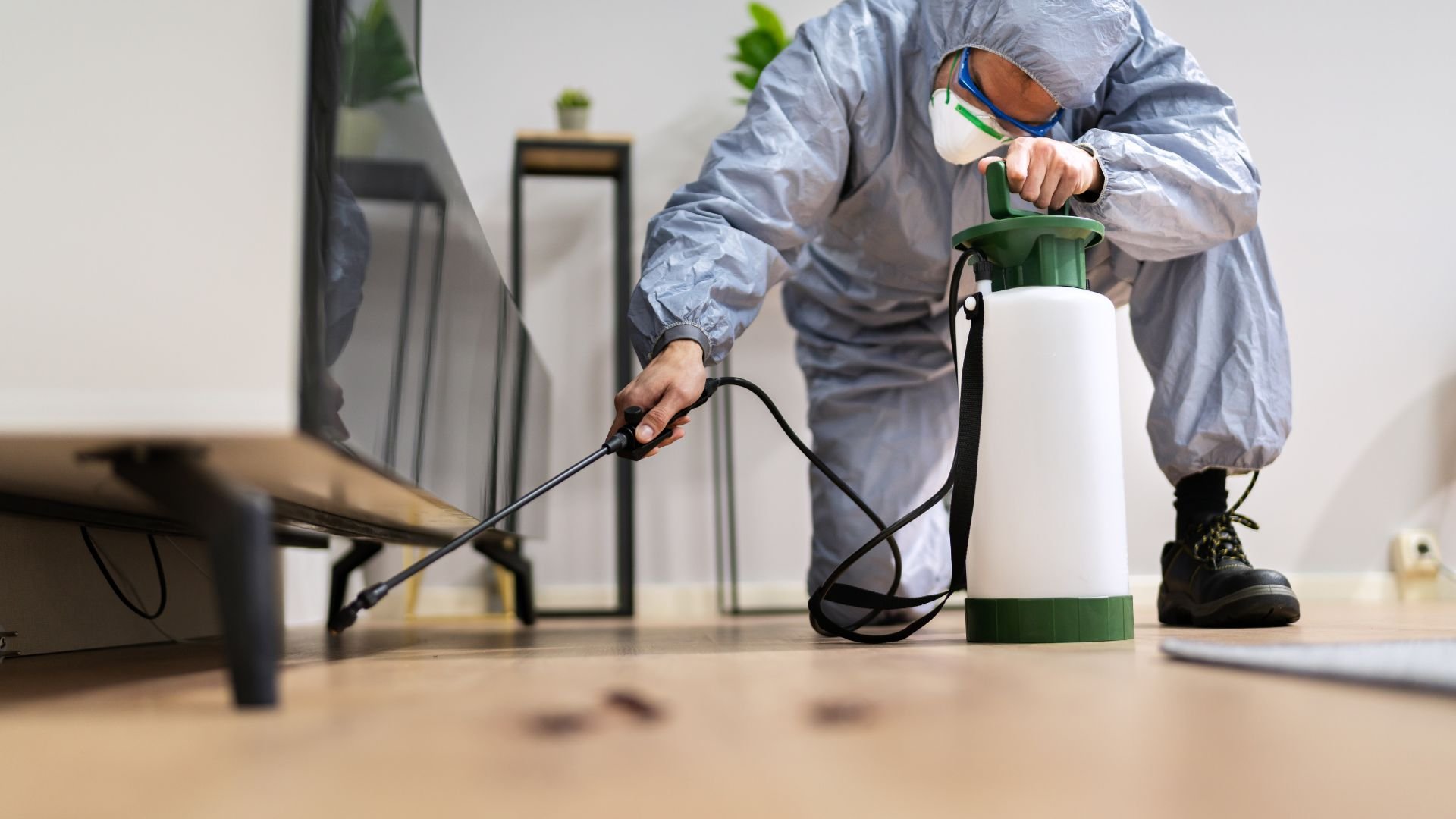 Person in protective gear using spray equipment for disinfection indoors